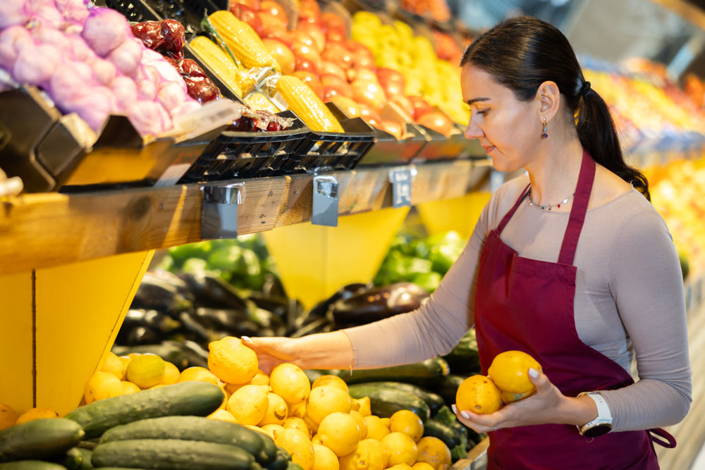 Female salesperson carefully places ripe lemons on the counter of grocery supermarket