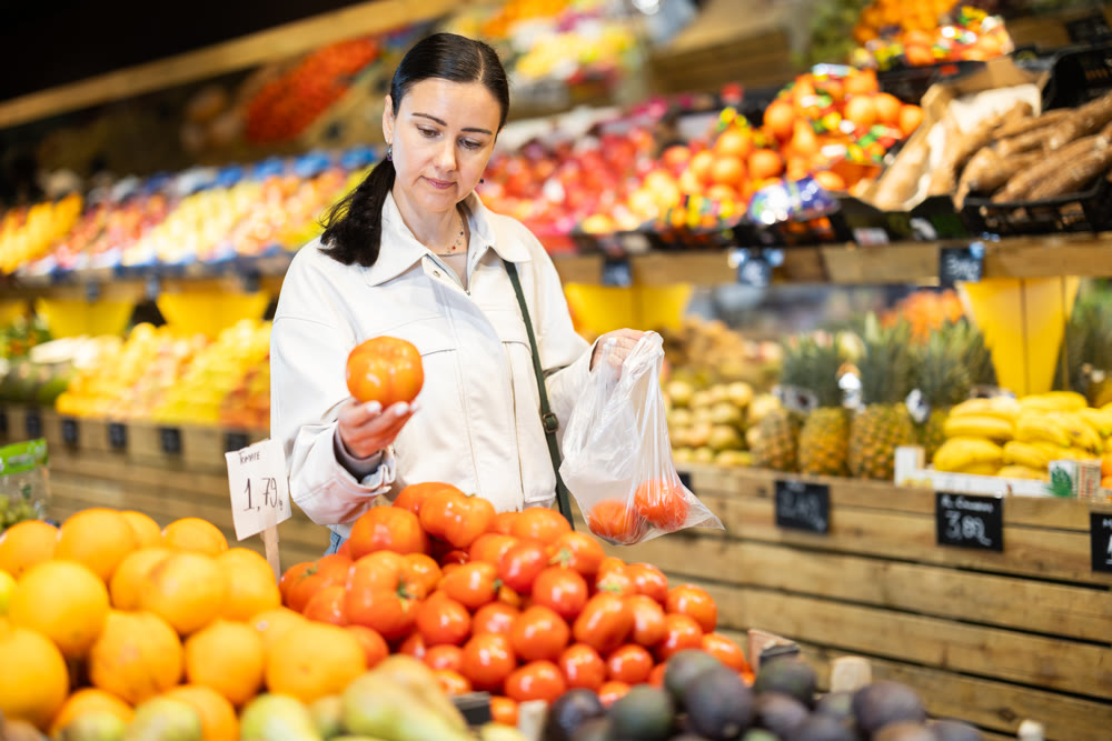 Woman carefully selects fresh tomatoes, standing near the counter in supermarket