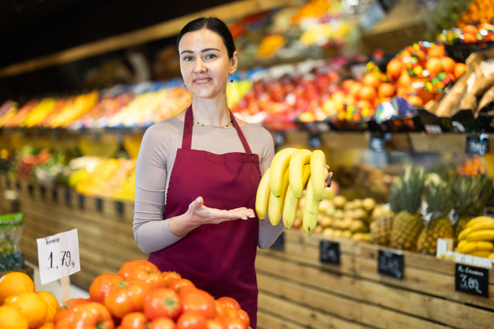 Middle-aged female seller offering bananas in grocery market
