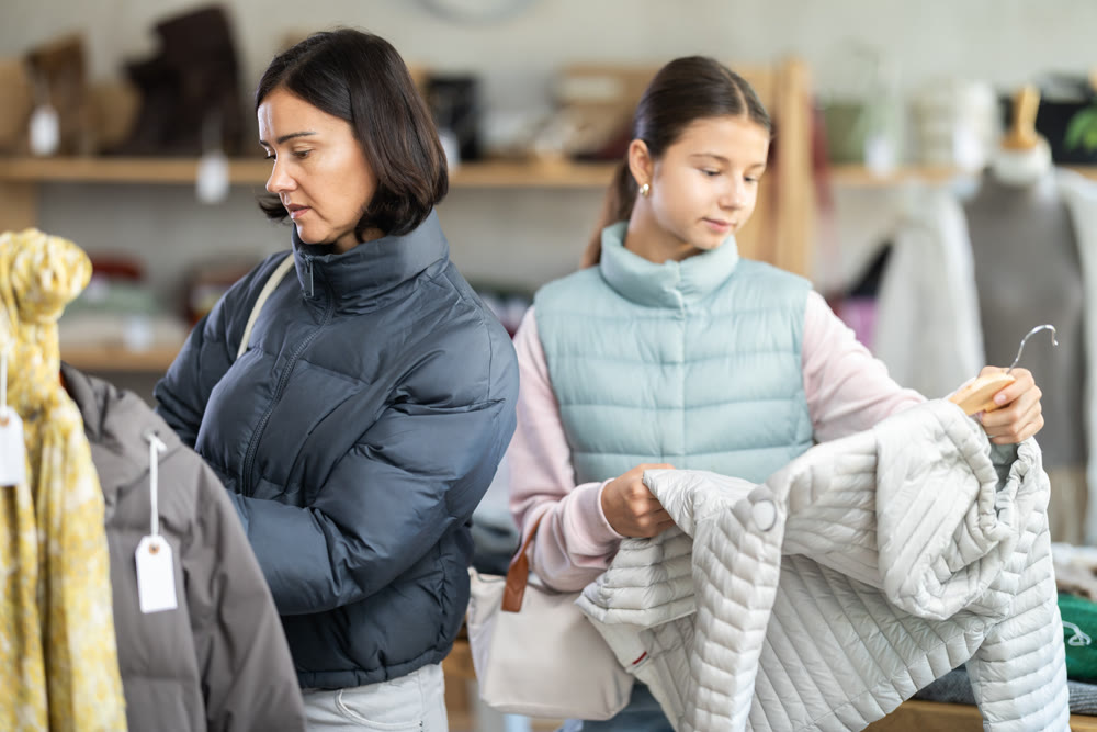 Mother and teen daughter looks at products in store and selects coat or jacket for child