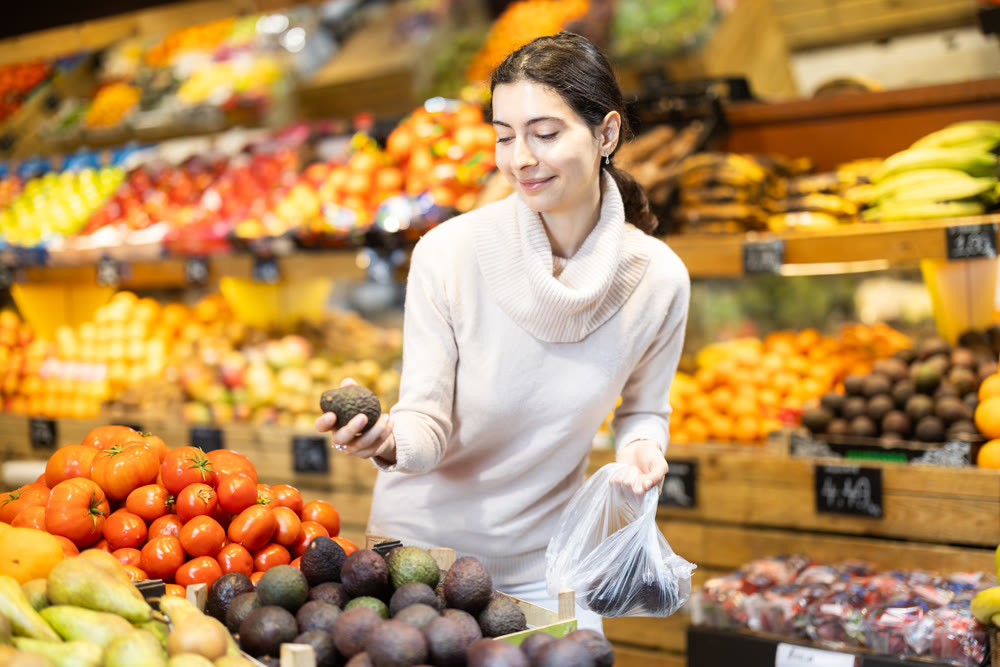 In vegetable store, young woman customer buy avocado