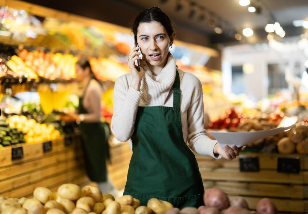 Woman seller takes inventory and talks on phone in vegetable store