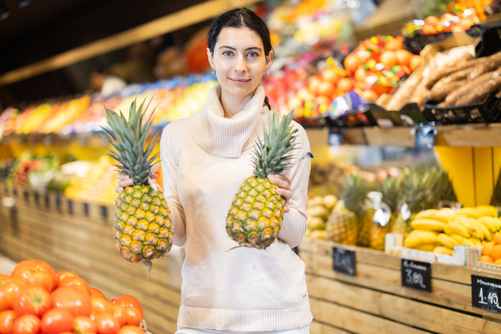 Young woman choosing pineapple in vegetable shop
