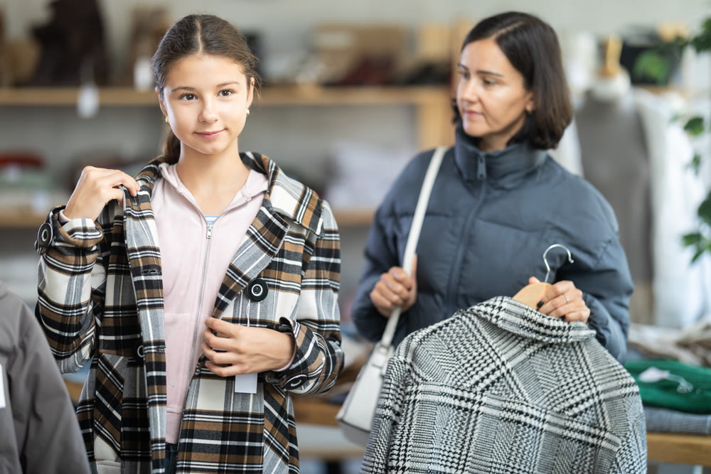 Adolescence girl try on plaid jacket during shopping with mother in clothes store