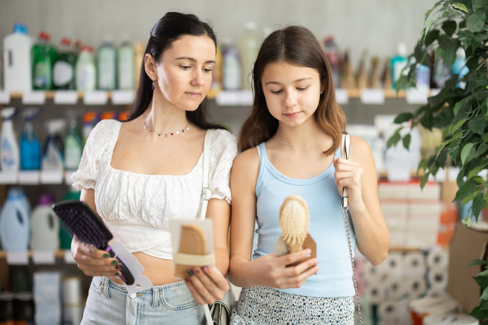 Mom and daughter choosing comb in store in summer