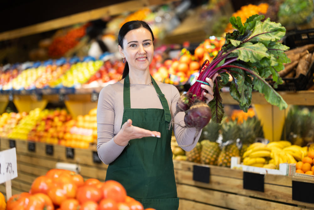 Middle-aged female seller offering beetroot in grocery market