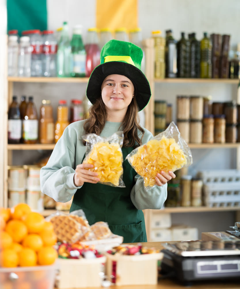 Positive teen girl store clerk in green hat is preparing to meet customers on eve of St. Patricks Day