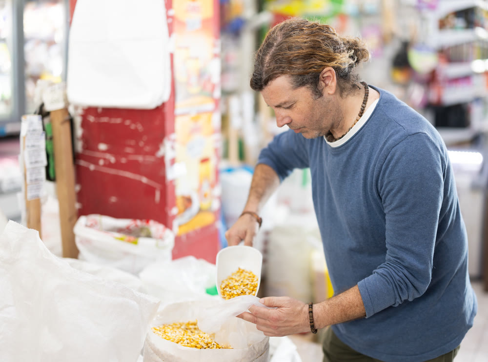 Adult man pours dry corn into bag at store