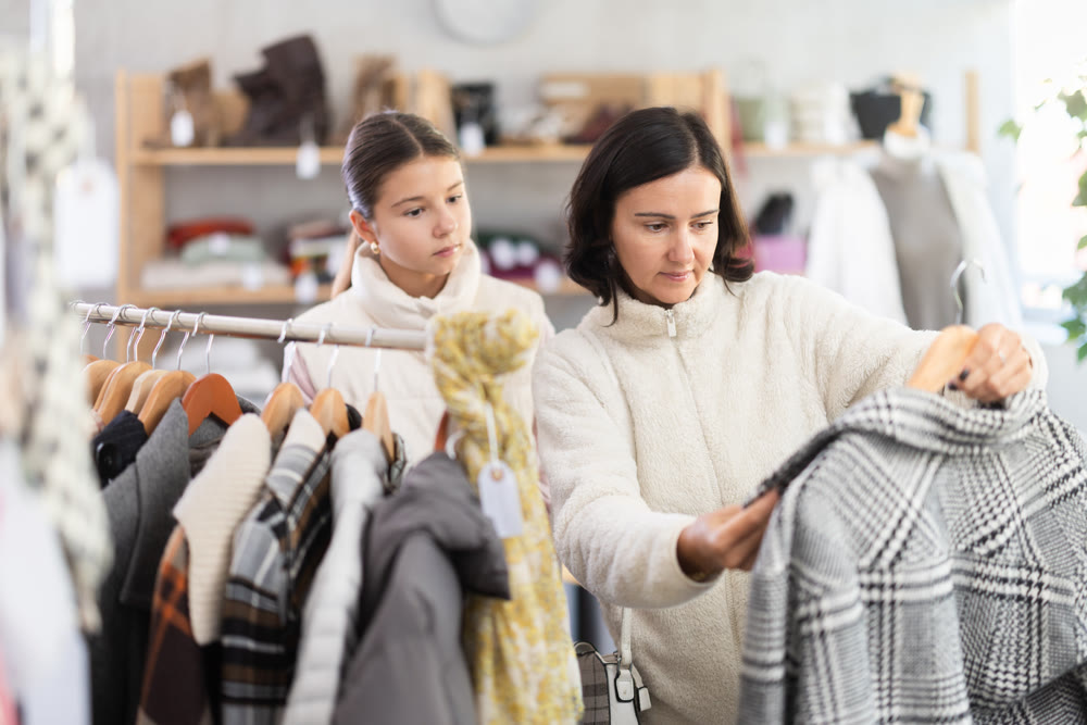 Mother and teen daughter looks at products in store and selects coat or jacket for child