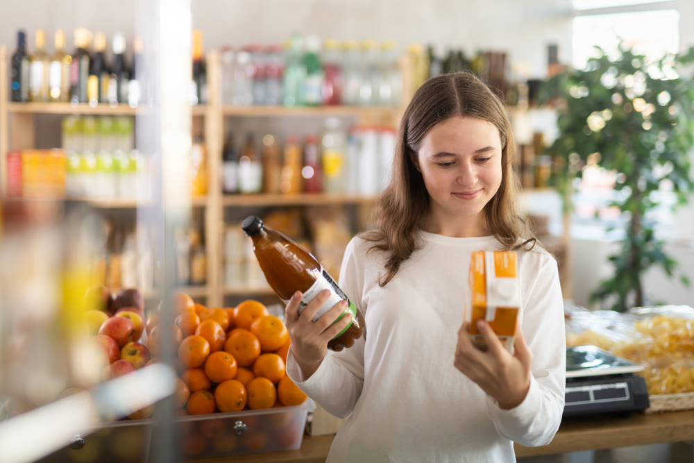 Teenage girl choosing peach and tomato juices at grocery