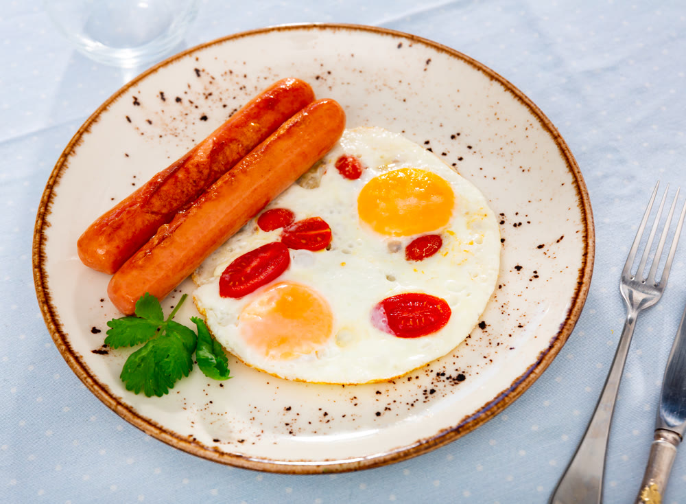 Homemade hearty breakfast - fried eggs with frankfurter and tomato