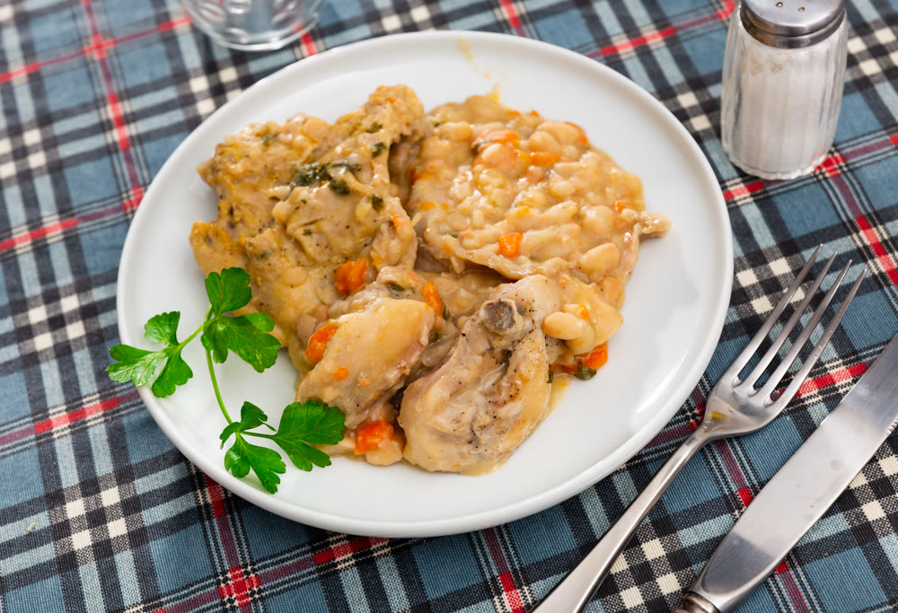 Oven-baked rabbit leg with braised beans in bowl, top view.