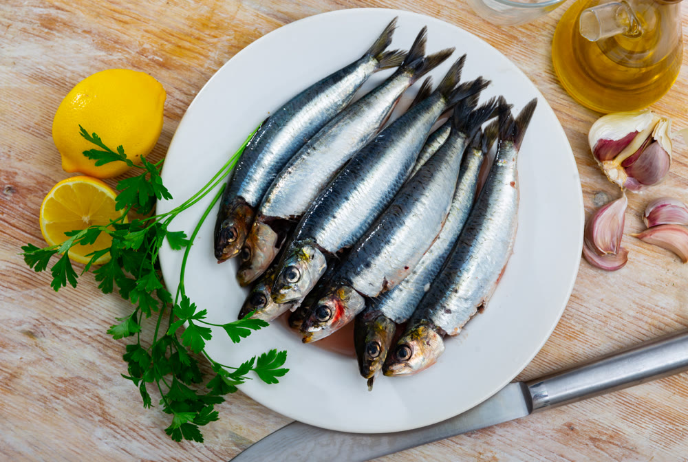 Raw sardines on plate with greens, lemon and garlic