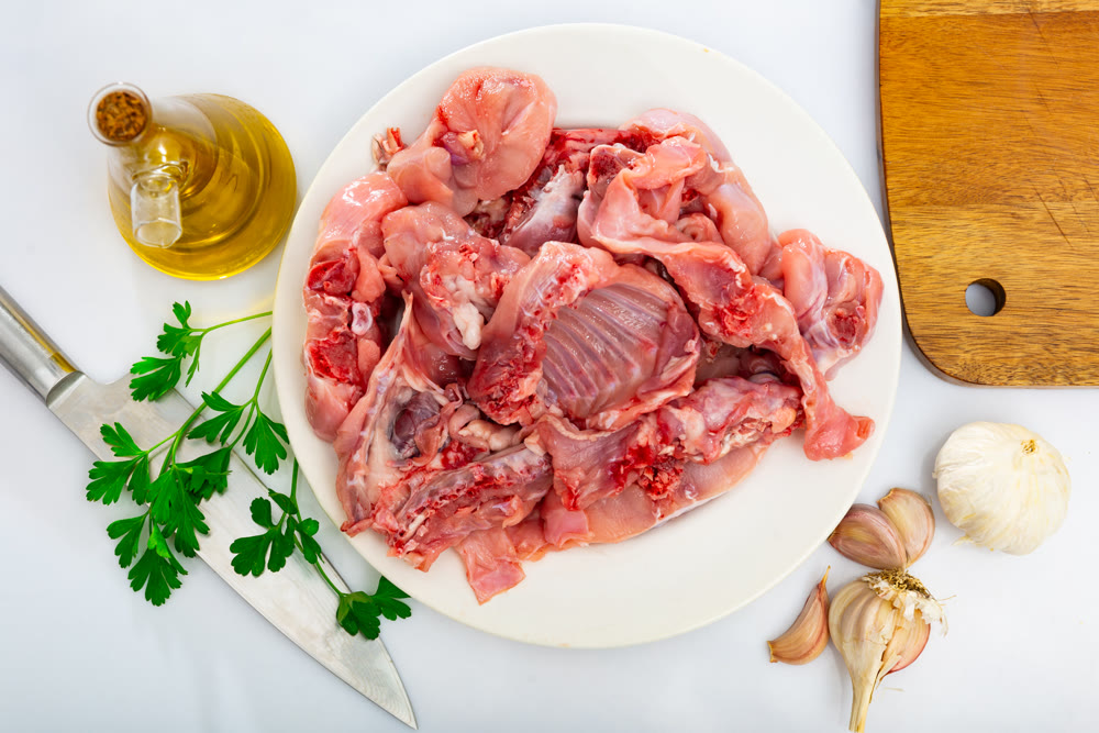 Plate with pieces of fresh raw rabbit, greens and condiments on table