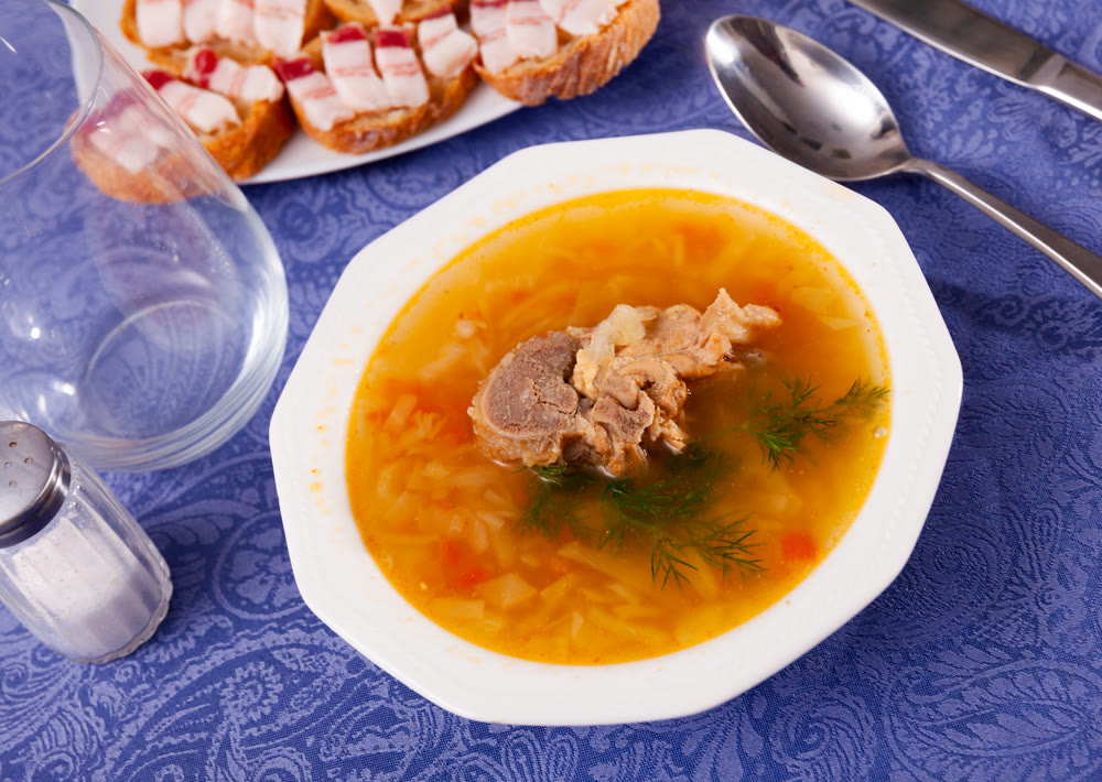 Fragrant cabbage soup decorated with dill. Dish is complemented with sandwiches with bacon