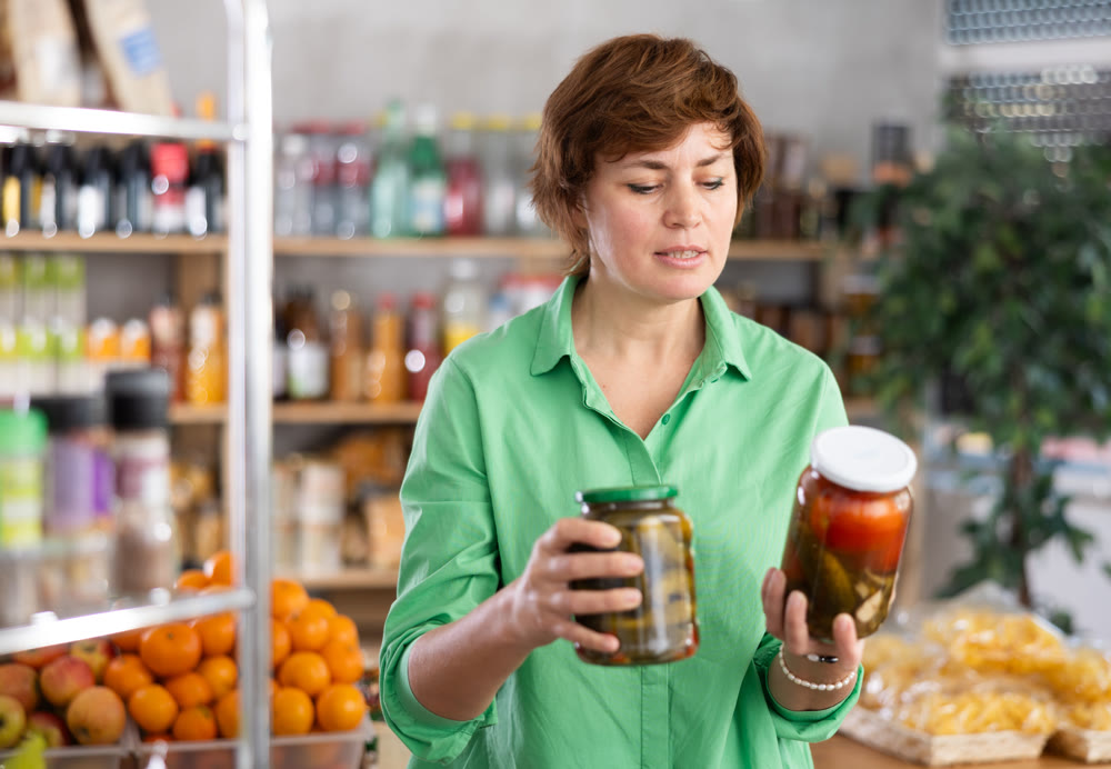 Female shopper selects pickled tomatoes in the produce section of supermarket