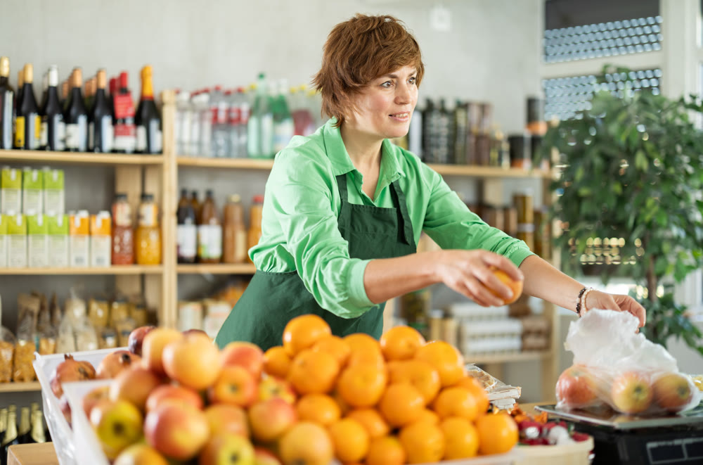 Positive female seller offers to buy apples and weighs them on scales