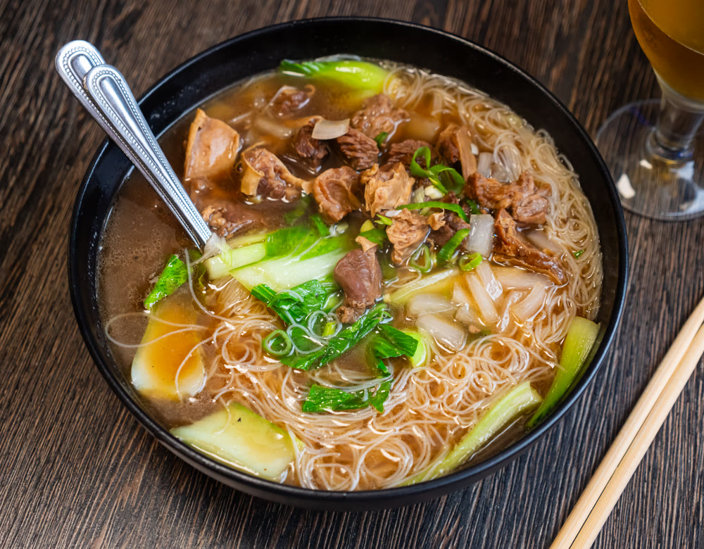 Deep clay bowl is filled with hot noodle soup and veal fillet.