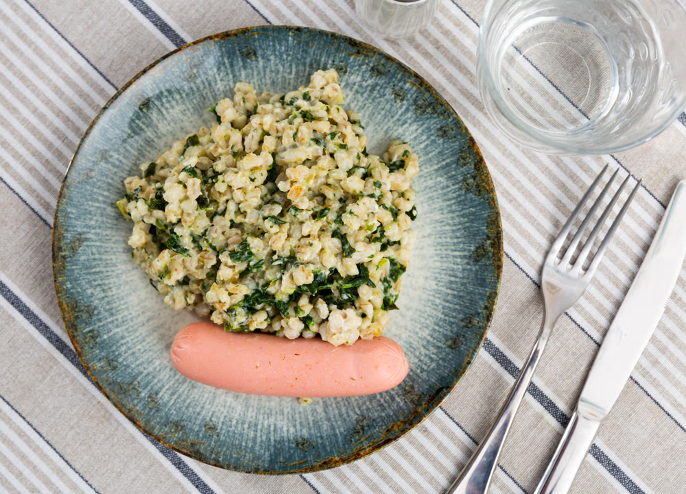 Boiled unpeeled sausage with side dish of pearl barley with spinach.