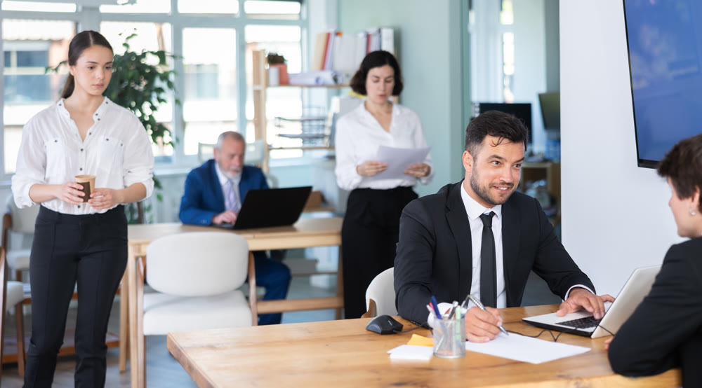 Professional adult male lawyer or bank employee talking and signing loan agreement with young guy client in bank office