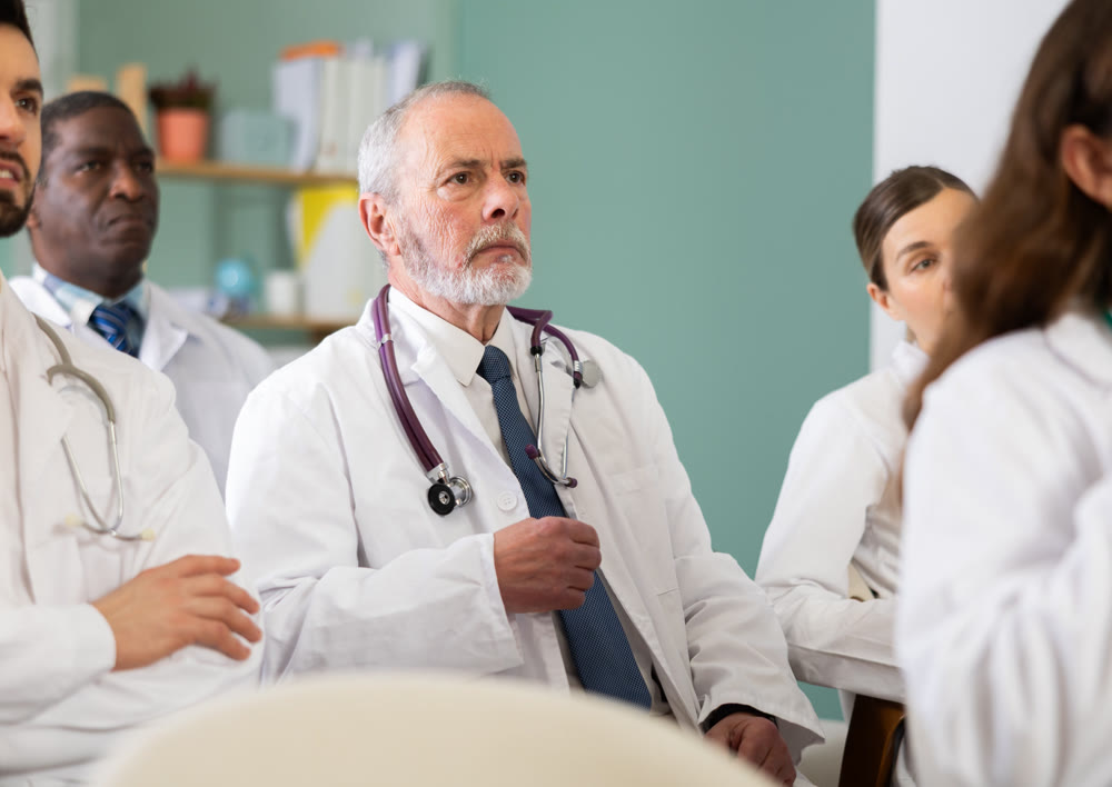 Mature man doctor student at courses meeting listens to teacher and look at speaker