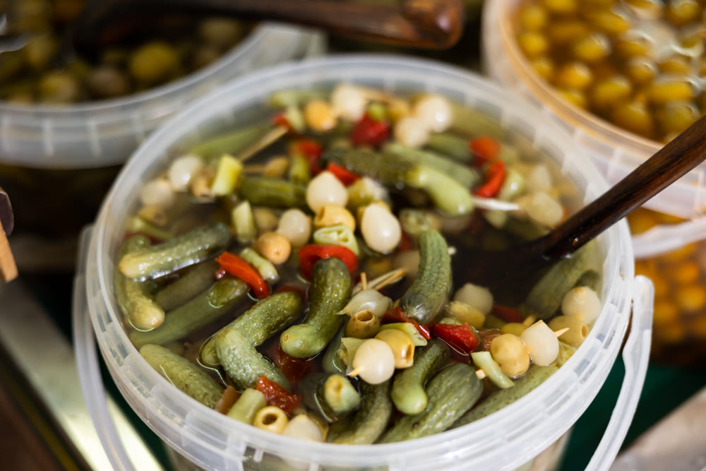 Marinated green olives, onions, cucumbers, peppers in a plastic container at market