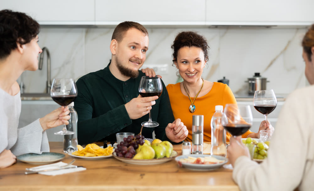 Group of happy celebrating holiday drinking and chatting at table at kitchen