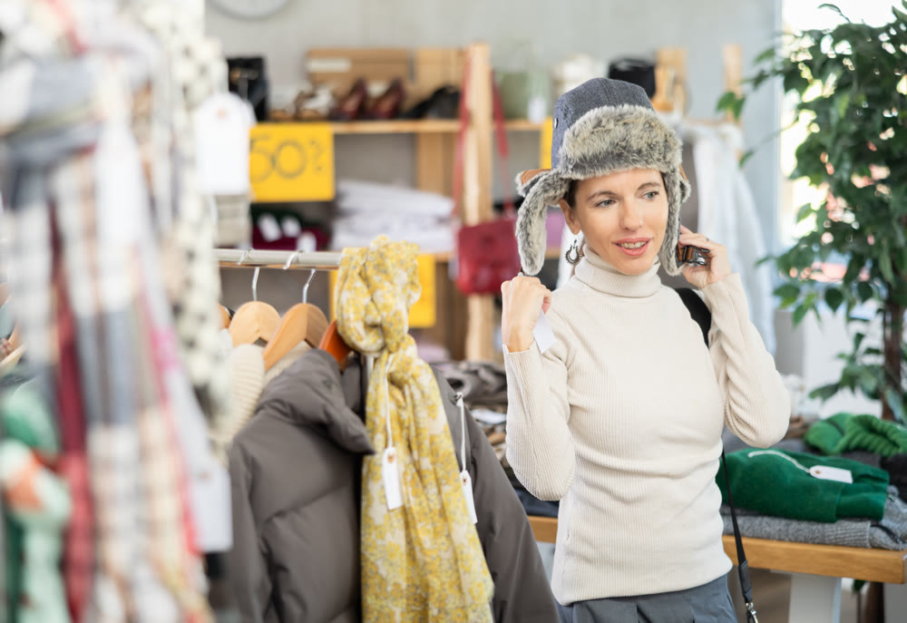 Glad middle-aged woman choosing fur hat in clothing store