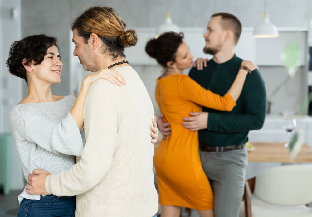 Four adult friends dancing and singing at home. Cheerful women and men enjoy music together. Happy people celebrating friendship