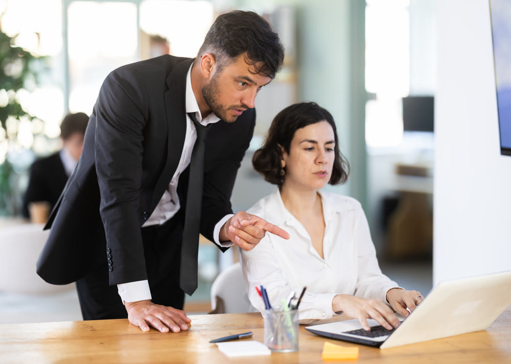 Attentive professional male co-workers helping new young female business worker with laptop, discussing new project in office