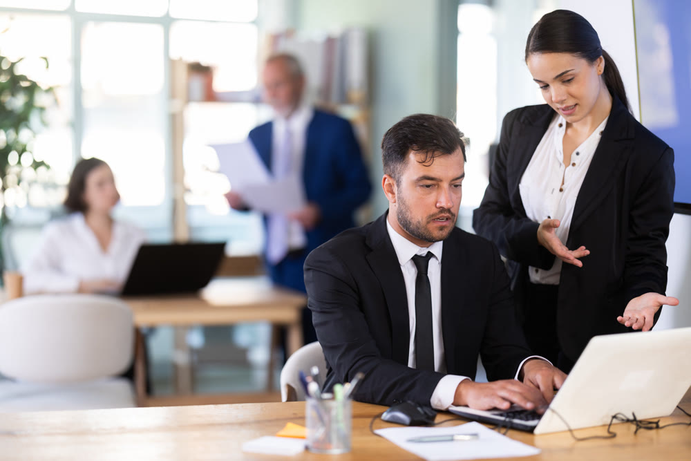 Woman head of a bank office stands with a male employee and helps with work issues