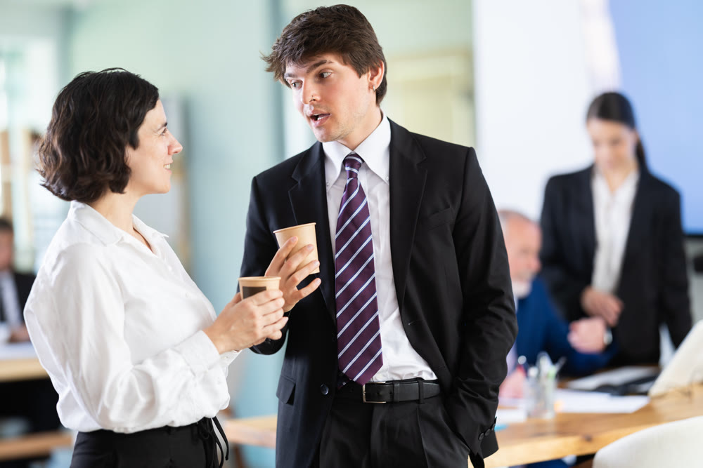 Young business woman and man co-worker employees drinking coffee and talking during break while working in office
