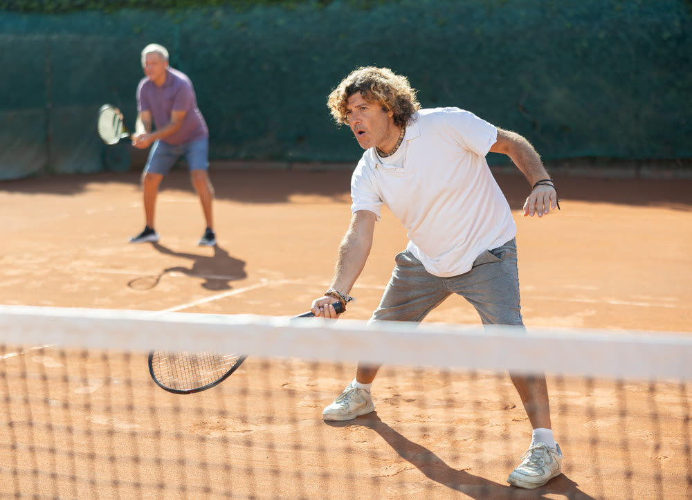 Two men in sportswear playing paddle tennis couple match on tennis courts, male player receiving hit from tennis racket