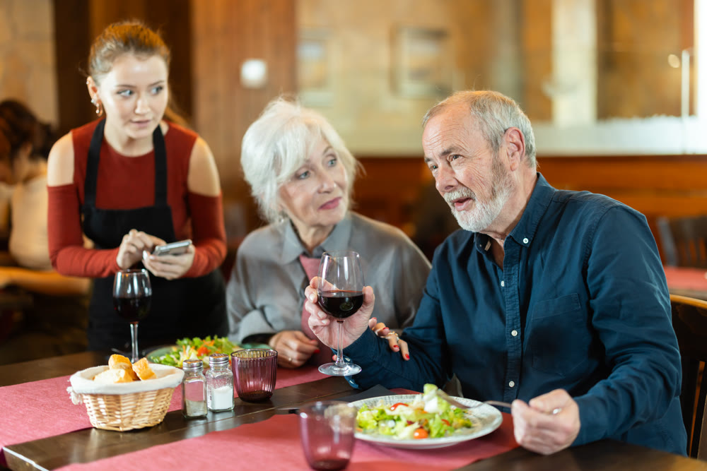 At cafe, girl waitress communicates with mature couple of customer, accepts order