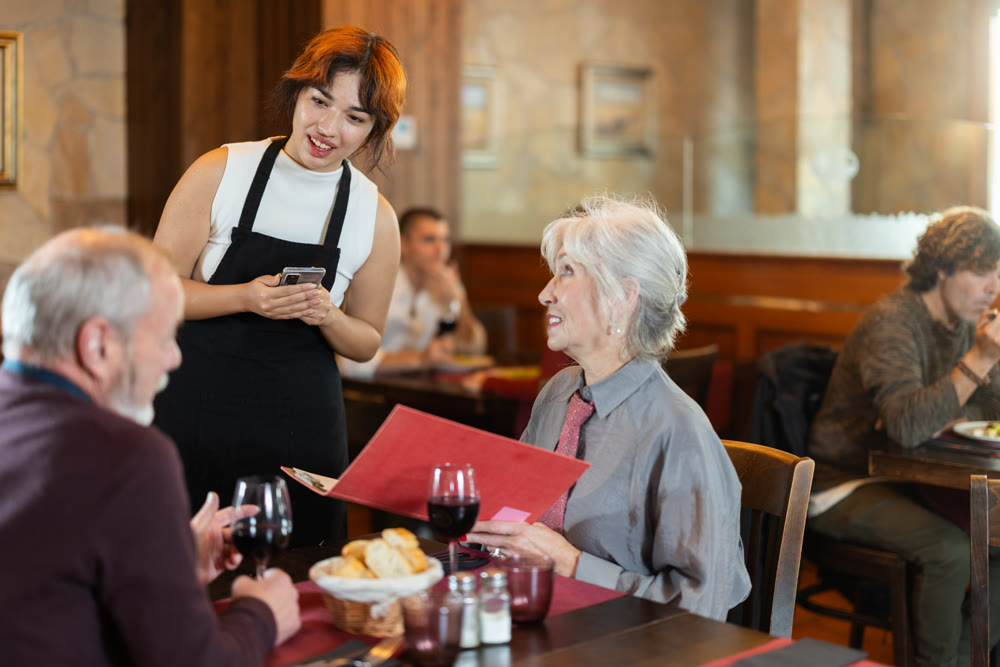 Young female waitress takes order from elderly couple