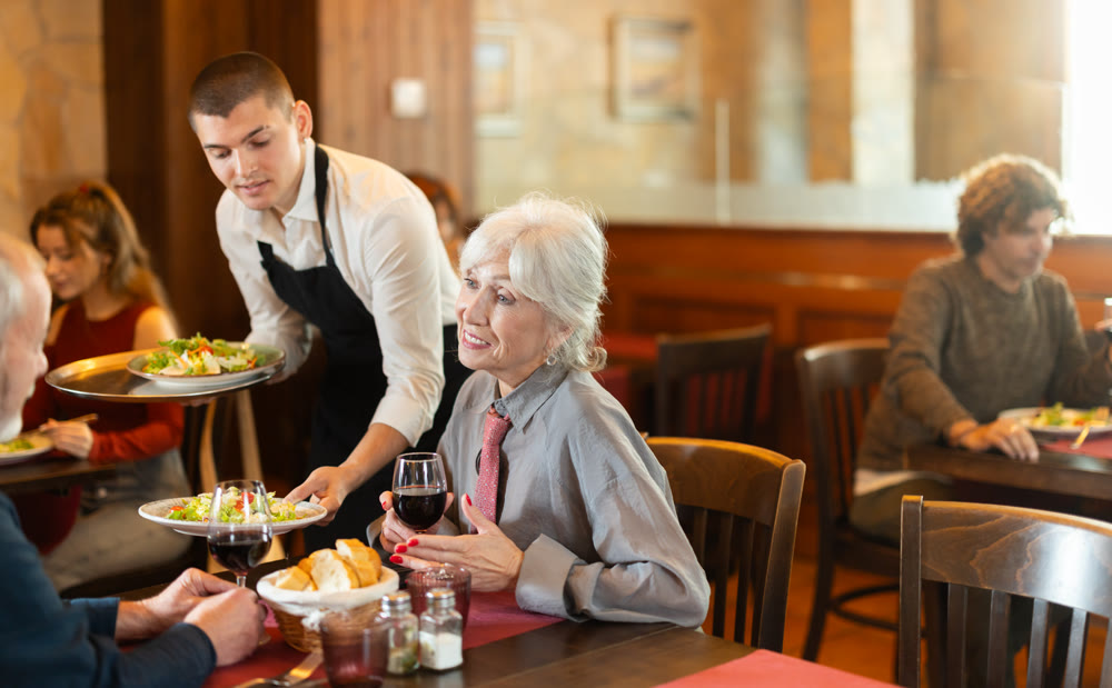 Waiter brings order to elderly man and woman couple
