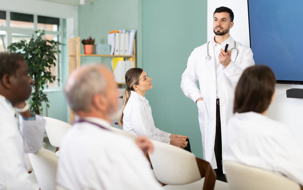 During lesson, male doctor with remote controller tell material, speaks to group of students