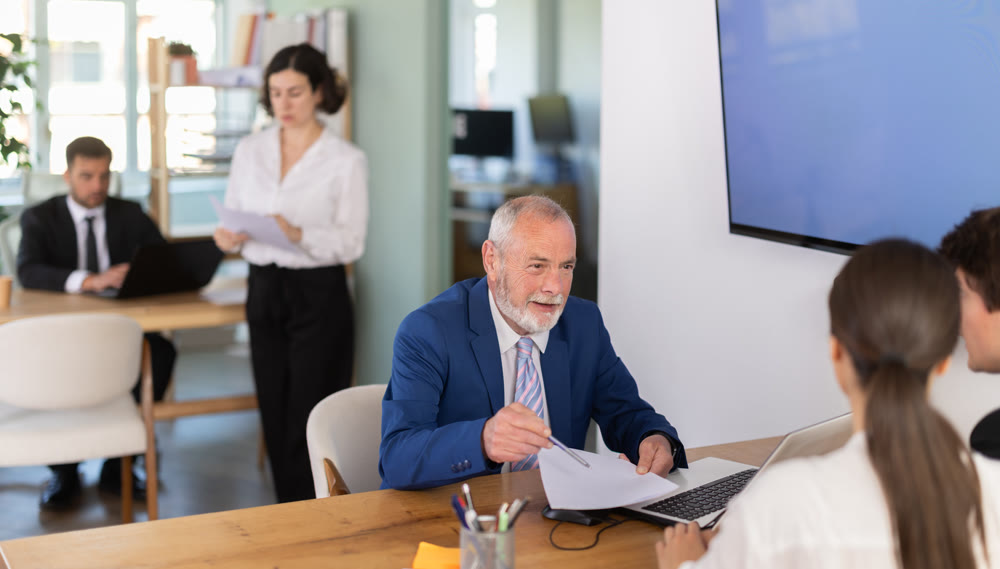 Professional mature male lawyer or bank manager talking with young couple and helping opening account in bank at office