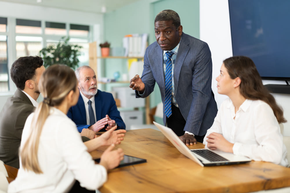 African man stands in front of business colleagues, tells report