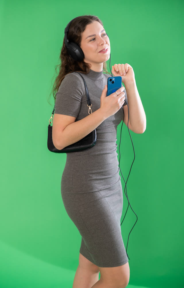 Young woman listening to music with headphones in front of green screen