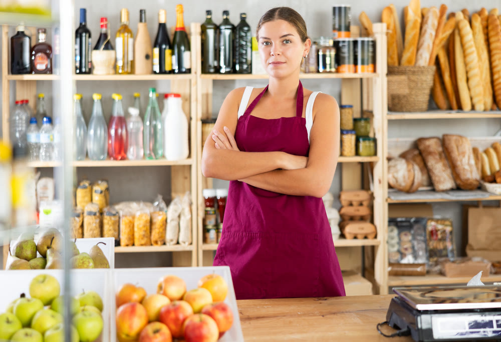 Portrait of smiling female salesperson in apron behind supermarket counter
