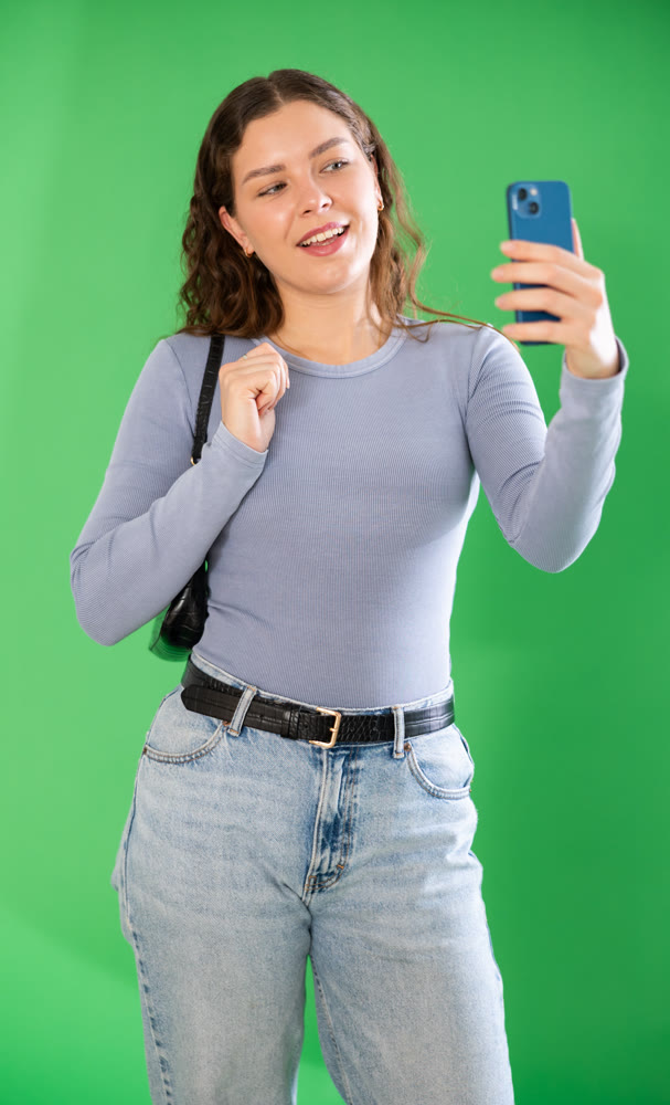 Young woman taking selfie in front of green screen