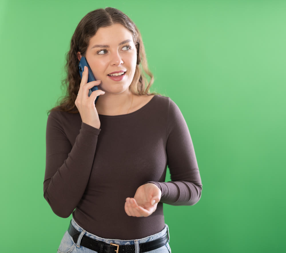 Young woman talking on mobile phone in front of green screen