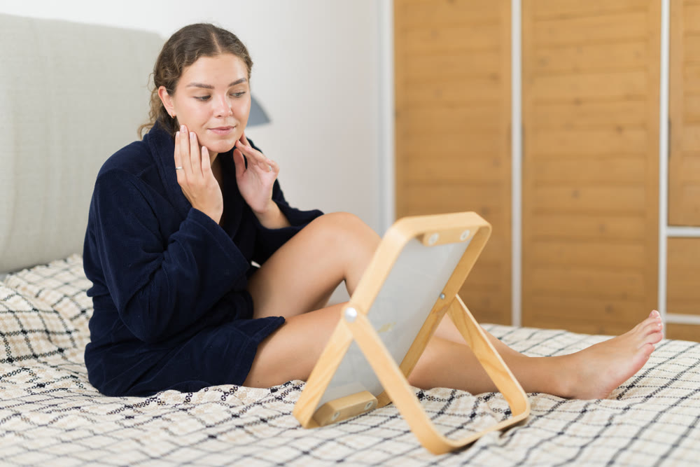 Woman in bathrobe looking in mirror in bedroom interior