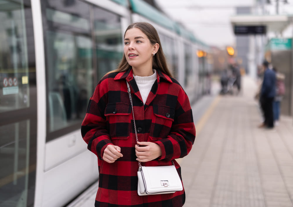 Girl is standing on street platform, waiting for tram to arrive