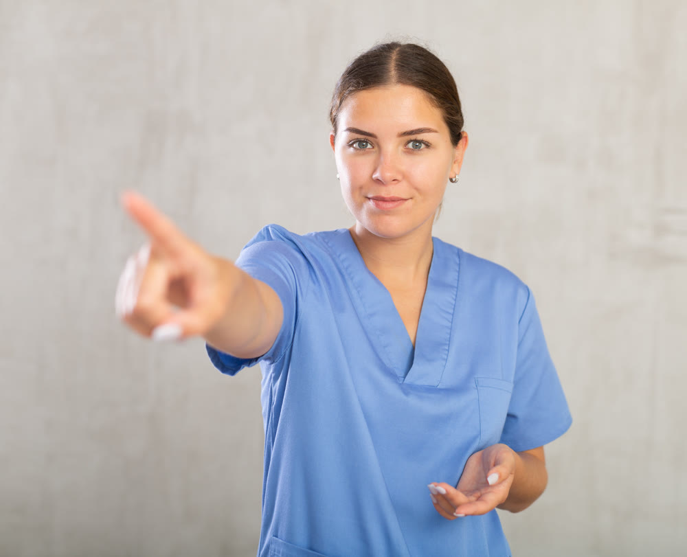 Young happy female nurse pointing somewhere with her finger