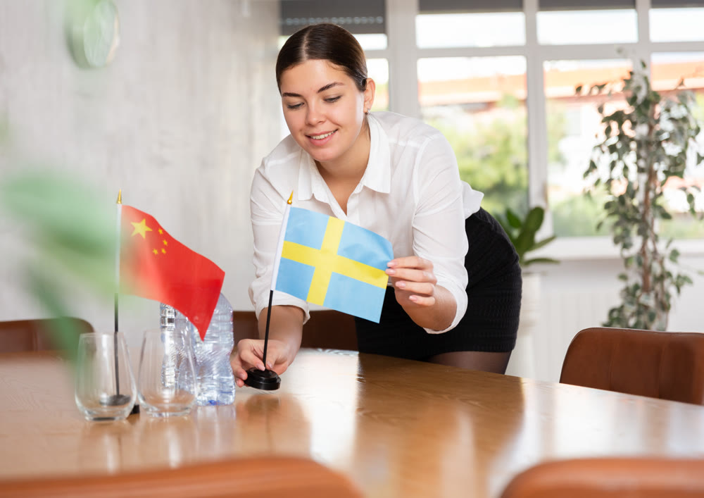 Preparing for business negotiations - woman sets small flags of countries of China and Sweden on table