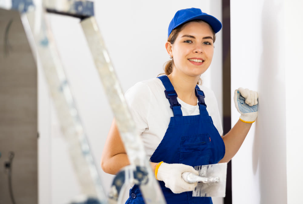 Portrait of young woman builder with trowel standing in apartment