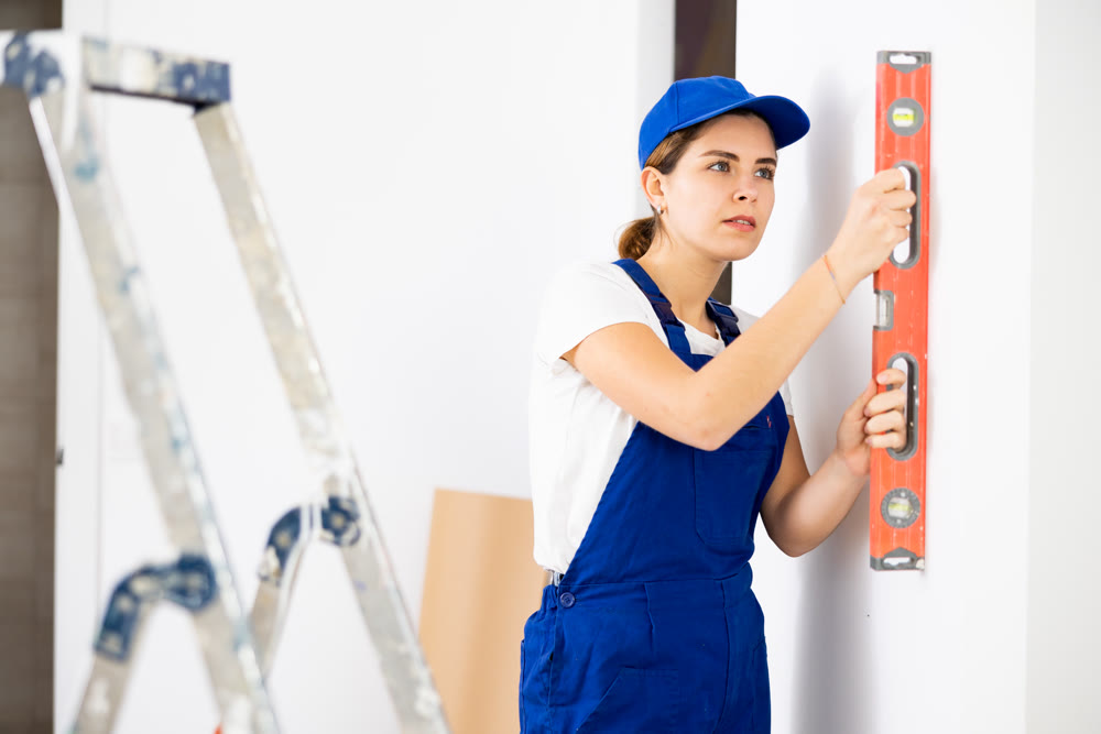 Woman builder using building level measures the vertical of wall