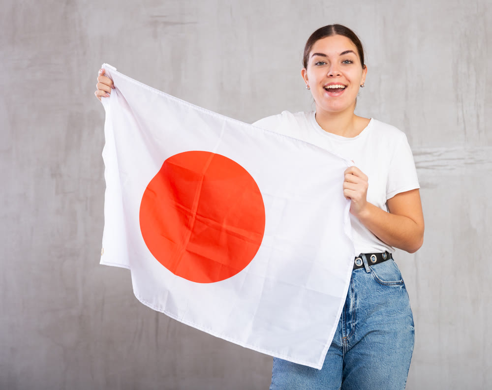 Joyous young woman holding Japan flag against unicoloured background